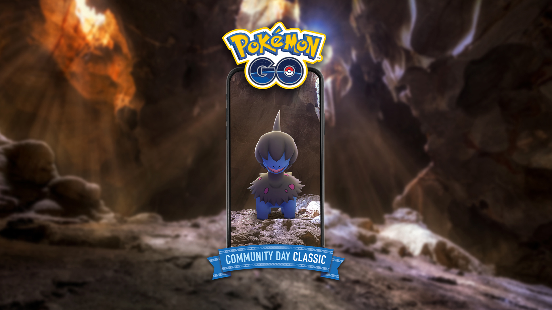 Un'immagine promozionale di Pokémon GO che mostra un Deino apparire sullo schermo di uno smartphone all'interno di una grotta buia e rocciosa.